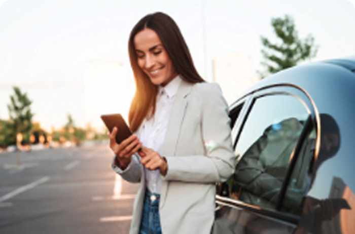 A woman looking at her mobile phone while leaning on a car.