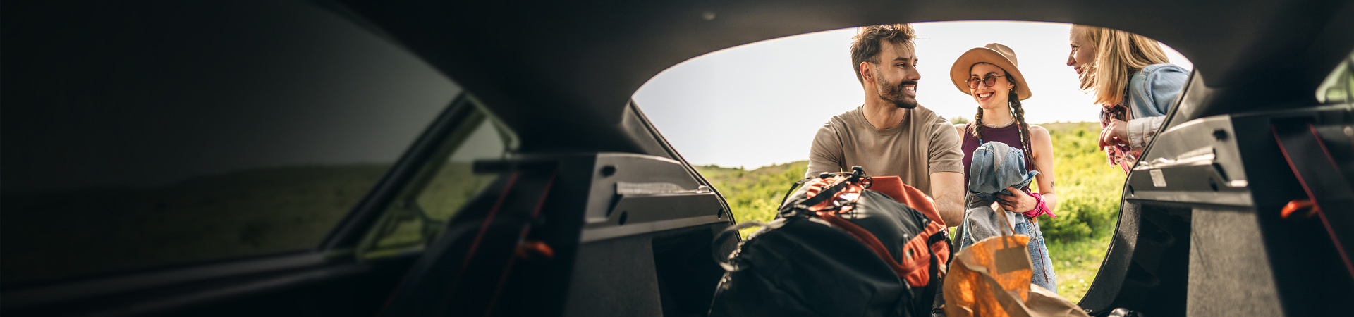 A man and a woman with waterproofs on getting some things out of a boot of a car. The sea and some mountains are in the distance.